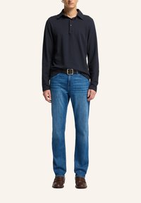 Polo a maniche lunghe blu navy, jeans blu e scarpe marroni. La camicia ha un collo e dettagli con bottoni; i jeans presentano una vestibilità classica.