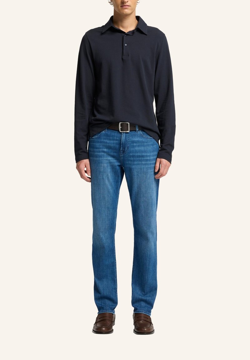 Polo a maniche lunghe blu navy, jeans blu e scarpe marroni. La camicia ha un collo e dettagli con bottoni; i jeans presentano una vestibilità classica.