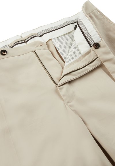 Beige Hose mit Reißverschluss und zwei braunen Knöpfen. Innenfutter mit gestreiftem Muster und sauberen Nähten. Glatte Textur, maßgeschneiderte Passform.