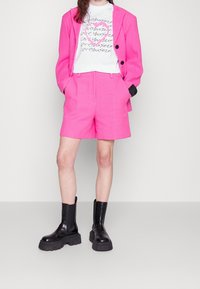 Lys pink blazer og shorts sæt med et struktureret mønster. Kombineret med en hvid t-shirt med håndskrevet sort tekst og kraftige sorte ankelstøvler.