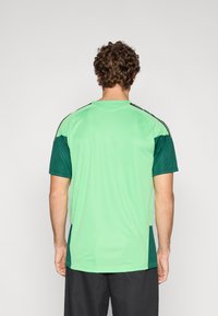 Green athletic jersey with short sleeves; features dark green accents and slim black stripes along the shoulders; smooth, lightweight fabric.