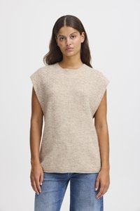 Beige kötött pulóver, bordás textúrával, rövid ejtett ujjakkal és kerek nyakkivágással, kék farmernadrággal viselve.