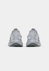 Graue Sportschuhe mit einem strukturierten Mesh-Obermaterial, gepolstertem Kragen, reflektierenden Akzenten und einer dicken, gepolsterten Sohle. Rückansicht.