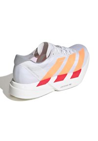 Bílé tenisky s oranžovými a červenými pruhy, texturovaný svršek, lehká konstrukce, polstrovaná podrážka označená "LIGHTSTRIKE PRO", minimální detaily značky.