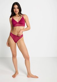 Bordeaux lingerie set met een bralette met kantafwerking en een stippenstructuur, gecombineerd met hoge taille slipjes, beide semi-doorzichtig.