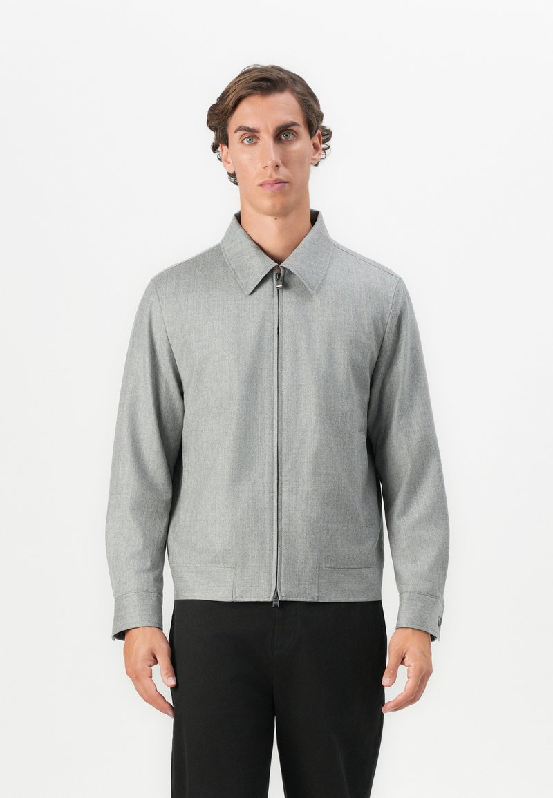 Gray zip-up jacket with a collared neckline, featuring smooth texture and side pockets, paired with black trousers.