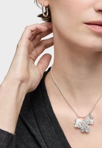 Collar de plata con cuatro charms: una flor texturizada, una flor lisa y dos piezas de acento, exhibido sobre un suéter oscuro.