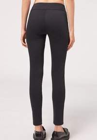 Svarta leggings i elastiskt material, med hög midja och smal passform, som slutar strax ovanför ankeln. Slät textur, utan mönster.