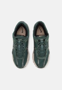 Tênis atléticos de malha verde com detalhes em preto, bico arredondado, atacadores e sola texturizada. Apresenta o logótipo da Nike na lateral e língua acolchoada.