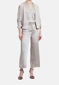Ljusgrå satin kostym med en kort blazer med vida ärmar och matchande vida byxor, båda med en jämn yta och subtil glans.