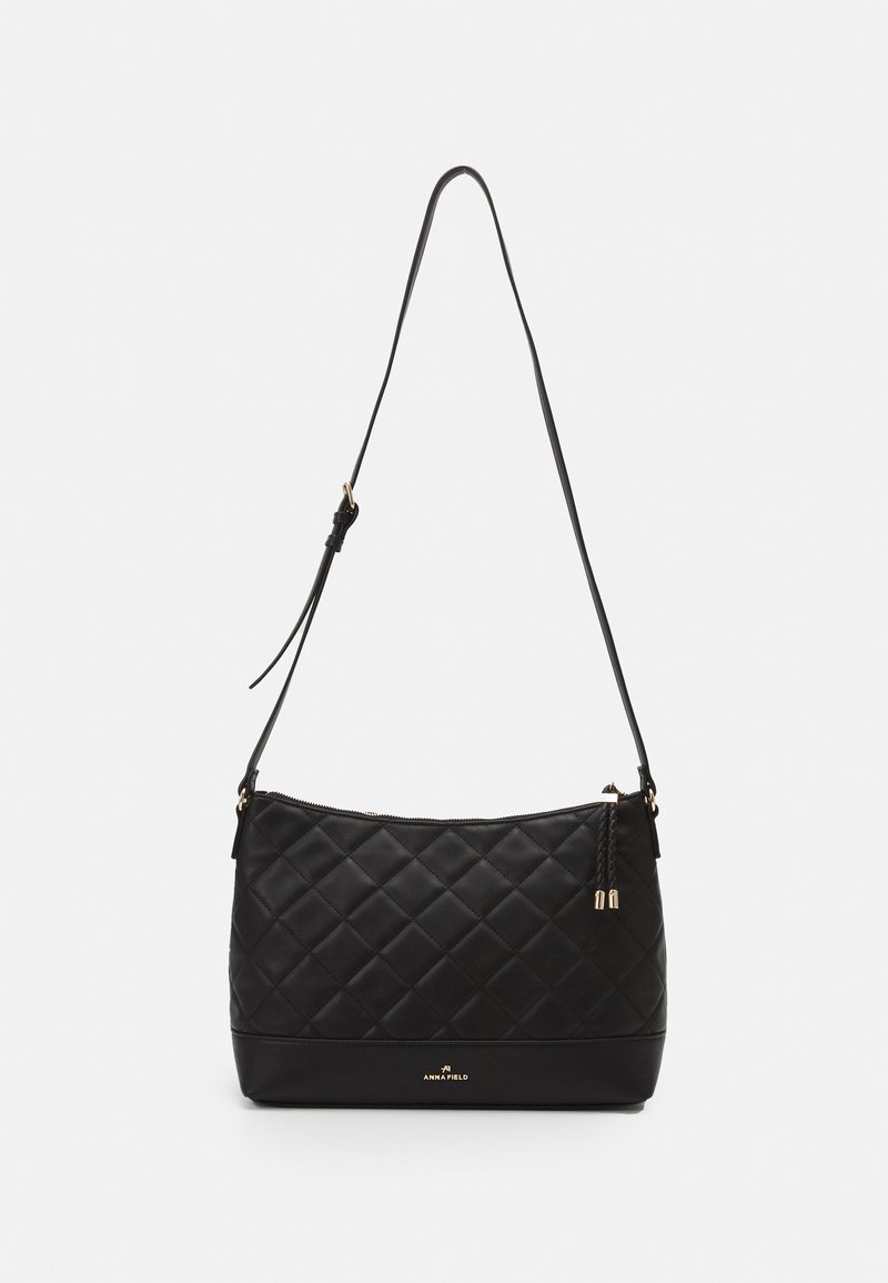 Musta tikattu olkalaukku, jossa on sileä pinta, kullanväriset metalliosat, säädettävä hihna ja vetoketjusuljin. Pohjassa näkyy brändäys.