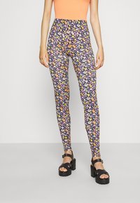 Legginsy w kwiaty z granatowym tłem i kolorowymi wzorami kwiatowymi; elastyczny pas; w połączeniu z czarnymi sandałami na platformie.