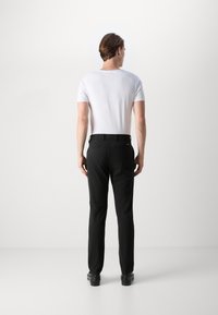Weißes Kurzarm-T-Shirt kombiniert mit schwarzen Hosen, die einen geraden Schnitt und dezente Taschen haben, von hinten betrachtet.