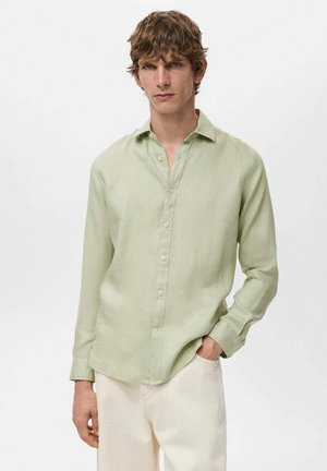 Camisa verde claro de manga larga hecha de tejido texturizado, con cuello y cierre de botones, metida dentro de pantalones de color claro.
