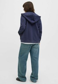 Felpa con cappuccio navy dal taglio rilassato, abbinata a jeans blu chiaro larghi e scarpe nere. Tessuto morbido e design informale.