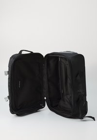 Black fabric bag with a rectangular shape, featuring a zippered opening, a logo tag inside, and dual carrying handles for transport.