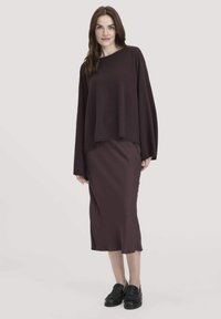 Burgunderfarbener, oversized Strickpullover mit langen Ärmeln, kombiniert mit einem passenden burgunderfarbenen Midirock. Schwarze Loafers runden das Outfit ab.