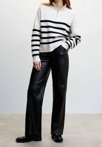 Weiß-schwarz gestreifter Strickpullover mit einem Reißverschluss am Kragen, kombiniert mit schwarzen, weit geschnittenen Lederhosen und schwarzen Schuhen. Glatte Texturen und ein strukturiertes Design.