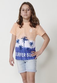 T-shirt s svetlo oranžovým a modrým gradientom obsahuje grafiku paliem a text "SURFER SOUL", doplnený o rolované džínsové šortky.