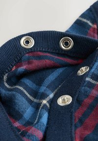 Granatowy dzianinowy produkt odzieżowy z srebrnymi zatrzaskami, podszewka wykończona tkaniną w czerwono-niebieską kratę z diagonalnymi paskami.