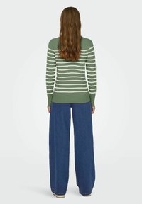 Pull rayé vert et blanc avec des manches longues, associé à un jean bleu à jambes larges. Texture en maille douce, ajusté à la taille, design décontracté.
