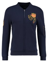 Chaqueta navy con cremallera hecha de una mezcla de algodón, que presenta parches bordados, cuello alzado, bolsillos laterales y un bolsillo en la manga con detalle de cremallera.