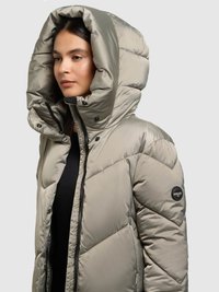 Polsterēta jaka gaiši pelēkā krāsā ar lielu kapuci, rāvējslēdzēja aizdari, diagonālu šuvju rakstu un apaļu logo uz piedurknes.