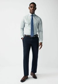 Lichtblauw en wit gestreept overhemd, marineblauwe broek, bruine riem en schoenen. Het overhemd heeft een standaard kraag en de broek is op maat gemaakt.