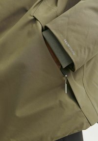 Olive spalvos švarkas su lygiu, matinio paviršiaus apdaila. Turėtų užtrauktukų kišenę su metaliniu traukikliu ir tekstūruotas rankogalius, pažymėtus „TECHFUSION“.