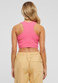 Rosa korte tanktopp med ribbestruktur og racerback-design, kombinert med beige bukser med elastisk liv som har sidelommer.