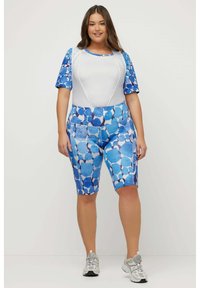Conjunto de ropa deportiva que incluye una camiseta blanca con mangas de patrón azul y pantalones cortos de talle alto en diferentes tonos de azul con formas geométricas.