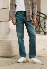 Jasnoniebieskie jeansy o prostych nogawkach, zestawione z białym t-shirtem i koszulą w kratę. Białe sneakersy dopełniają strój.