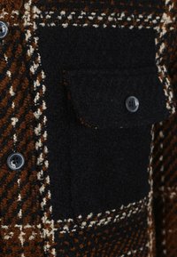 Geruite wollen jas met bruin en zwarte patronen, met een gestructureerd oppervlak, zwarte knoopsluiting en een borstzak aan de voorkant.