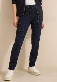 Joggeurs en imprimé léopard marine, fabriqués en matériau doux, avec une taille élastique et un cordon de serrage ; associés à des baskets blanches.