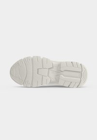 Semelle de chaussure blanche avec des rainures profondes et des motifs texturés antidérapants, vue de dessous sur un fond clair uni.
