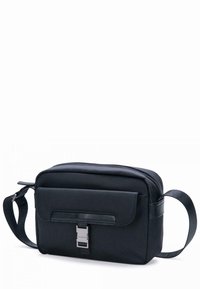 Borsa a tracolla nera in nylon, forma rettangolare, dotata di chiusura con zip, pattina frontale con snap e tracolla regolabile. Texture liscia con dettagli in metallo.