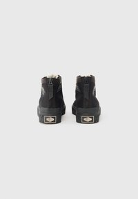 Bottines montantes noires avec une semelle en caoutchouc texturé, dotées d'une fermeture éclair et d'une étiquette de logo. La tige a une finition en tissu lisse avec des coutures d'accent.