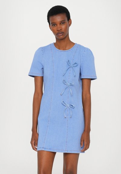 Denim dress in light blue with short puff sleeves, round neckline, and three bow details on the front. Smooth texture with contrast stitching.