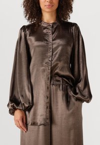 Bronzen satijnen blouse met lange pofmouwen, knoopsluiting aan de voorkant en bandkraag; heeft een soepele textuur en een relaxte pasvorm.