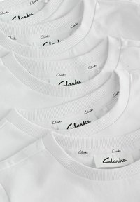 Neli valget t-särki ribaga ümarate kraega, millel on mustades siltides kaeluses nööbitud "Clarks" logo.
