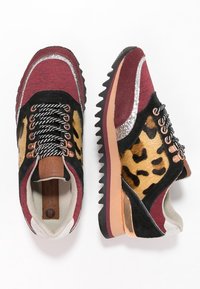 Sneaker bicolore con tessuto testurizzato rosso e nero, dettagli in stampa leopardata, rifiniture metalliche e suola in gomma resistente.