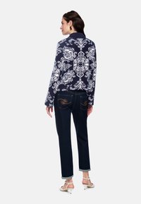 Navy patterned sweater with white floral design, paired with dark denim jeans, cuffed at the ankles. Model wears white strappy heels.