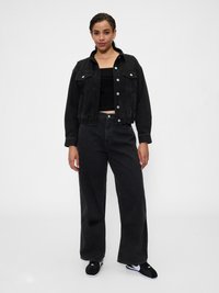 Casaco de ganga preto com dois bolsos frontais e botões prateados, combinado com jeans pretos de cintura alta e sapatilhas pretas. Textura suave.