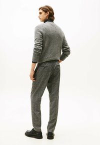 Suéter gris texturizado con puños acanalados, combinado con pantalones gris a juego. Zapatos negros completan el look. Tomado desde la parte trasera.