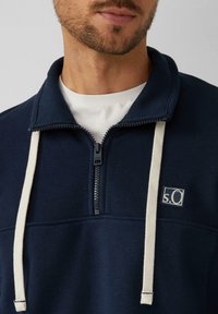 Sudadera navy con media cremallera, elaborada con tejido texturizado y cordones blancos en contraste, que presenta un pequeño logo en el pecho.