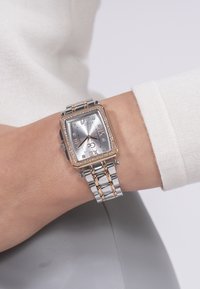 Handled med ett tvåfärgat armbandsur i silver och roséguld som har en rektangulär urtavla med romerska siffror samt kristallaccenter på bezel och urtavla.