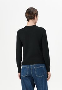 Svart strikket genser med lange ermer, ribbet nederkant og en enkel rund halslinning, kombinert med høytlivs blå denimjeans.