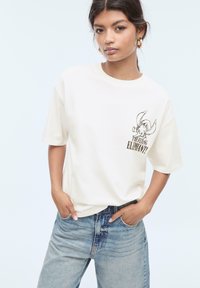 T-shirt en coton blanc à manches courtes avec un graphique noir d'un éléphant et le texte "L'ÉLÉPHANT VOLANT !" à l'avant.