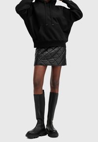 Black oversized hoodie, quilted black leather mini skirt, and knee-high black boots with thick soles, set against a light gray background.