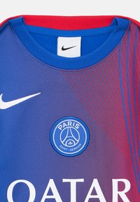 Maillot Nike arborant un dégradé de violet à rouge, avec un logo PSG rond en bleu, et le célèbre swoosh en blanc. Le texte "QATAR" est inscrit en dessous.